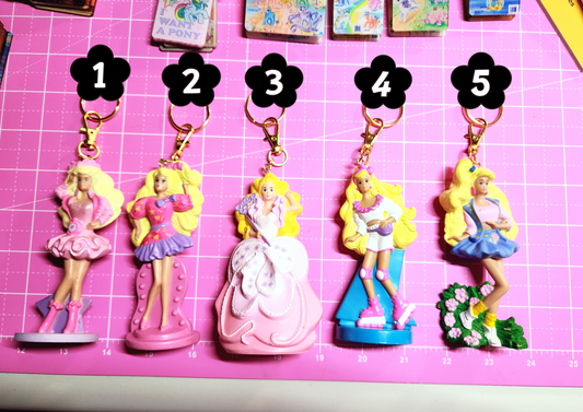 Set of five Barbie-themed keychains on a pink grid background