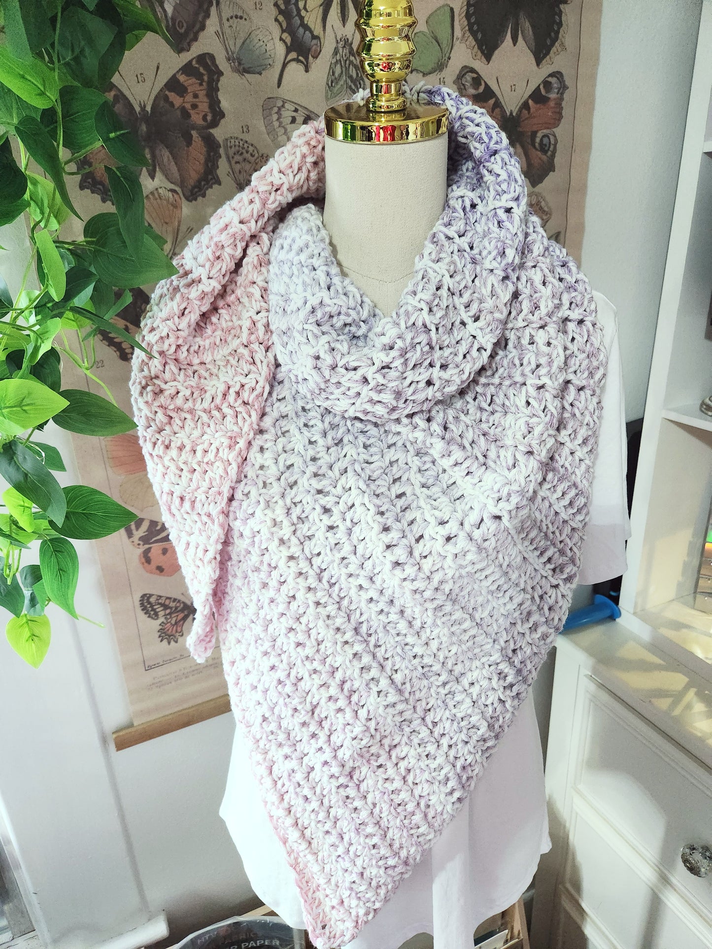 Mannequin wearing a pink and white crocheted shawl with butterfly wallpaper in the background