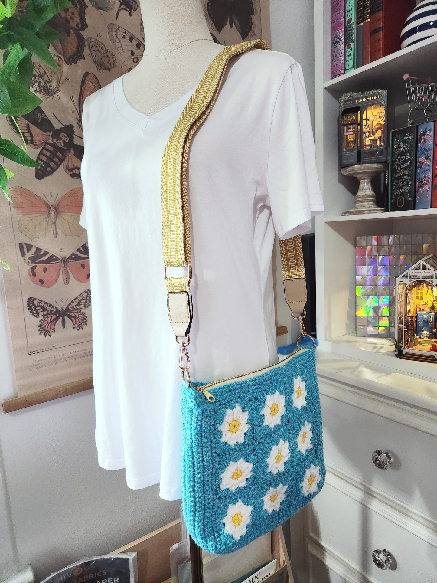 Mannequin wearing a white shirt with a blue floral-patterned crossbody bag in a room with decorative items.