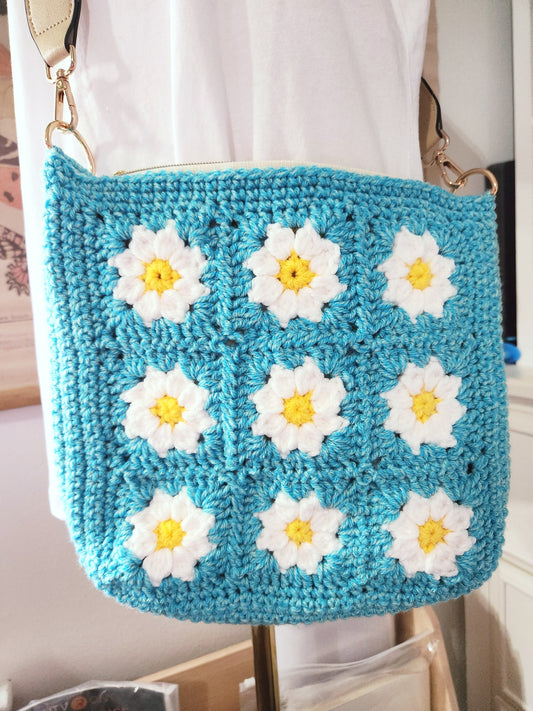 Blue crochet bag with white daisy patterns on a white background