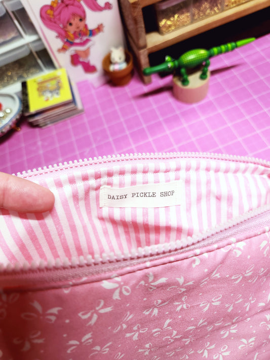 Pink fabric with floral pattern and zipper, held by a hand on a pink background.