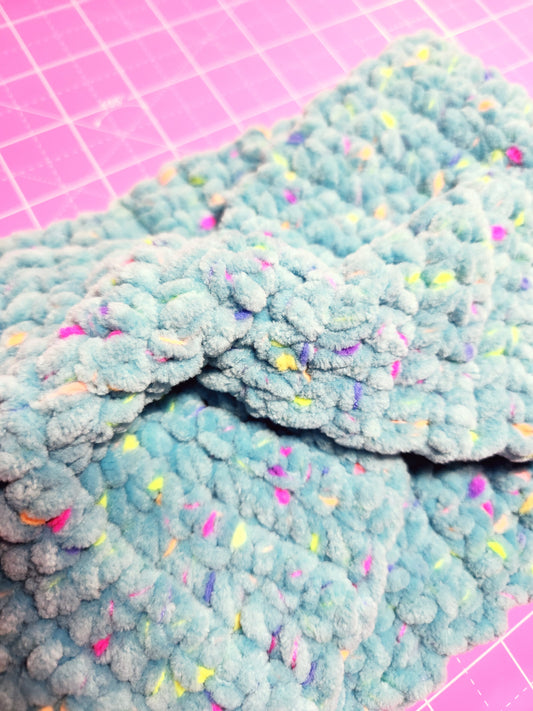 Blue textured material with colorful specks on a pink grid background