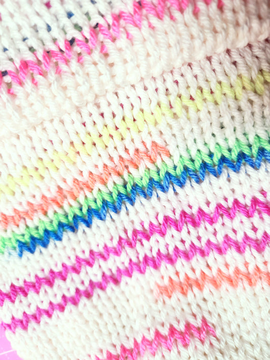 Close-up of colorful knitted fabric with pink, blue, green, and white yarn.