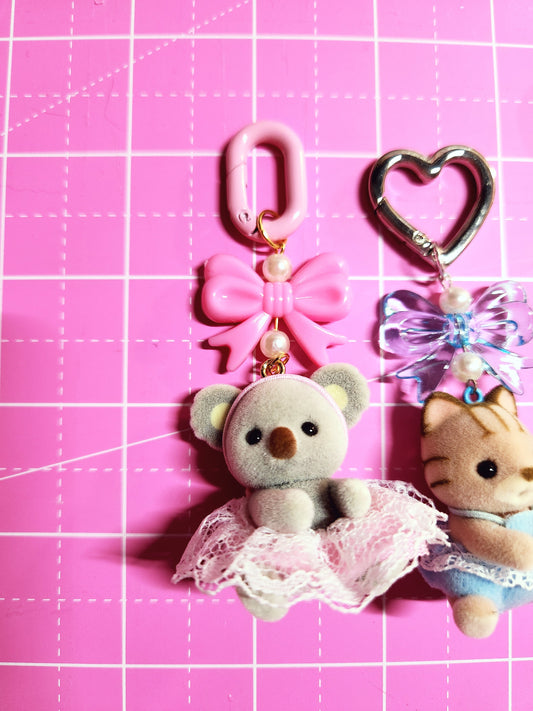 Small teddy bear keychain with pink bow and heart-shaped clip on a pink grid background