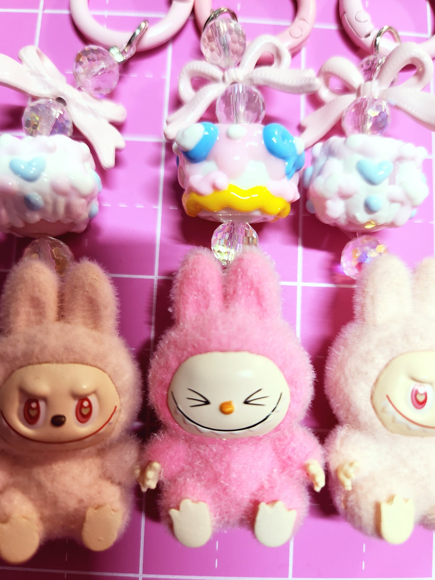 Cartoonish plush toys with colorful beads on a pink grid background