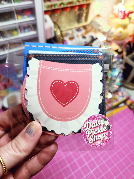 Hand holding a small pink book with a heart design and 'Double Happiness' sticker against a blurred background.