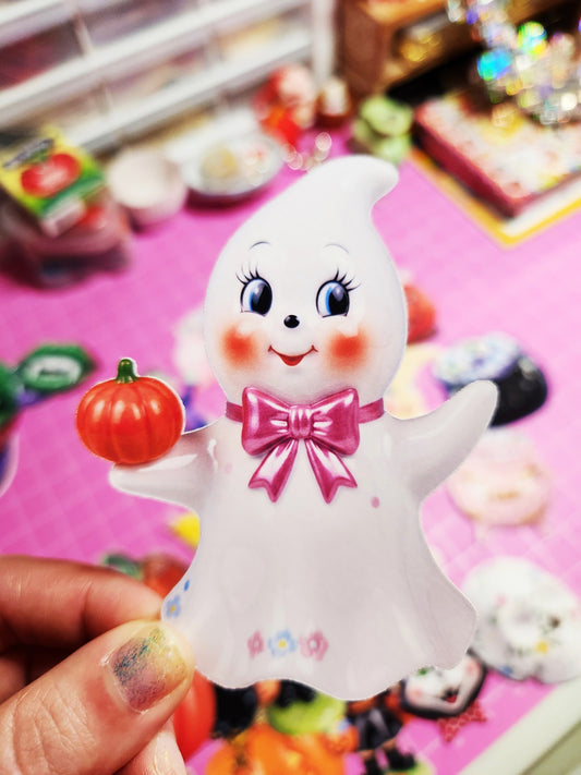 Toy ghost figure with a pink bow and pumpkin held by a hand on a colorful background
