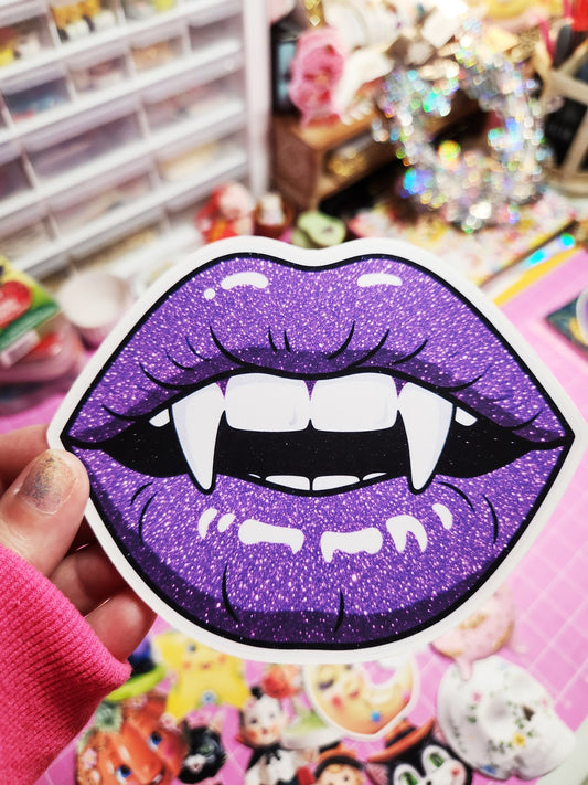 Sticker of purple glittery lips with fangs held in front of a colorful background.