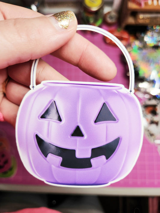 Purple Halloween candy container with a pumpkin face design held by a hand.