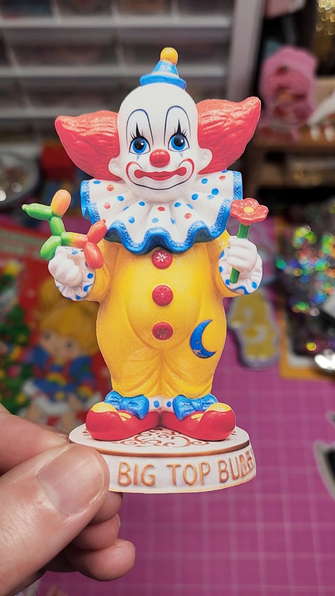 Clown figurine with colorful outfit and 'Big Top Bubbles' text held by a hand.