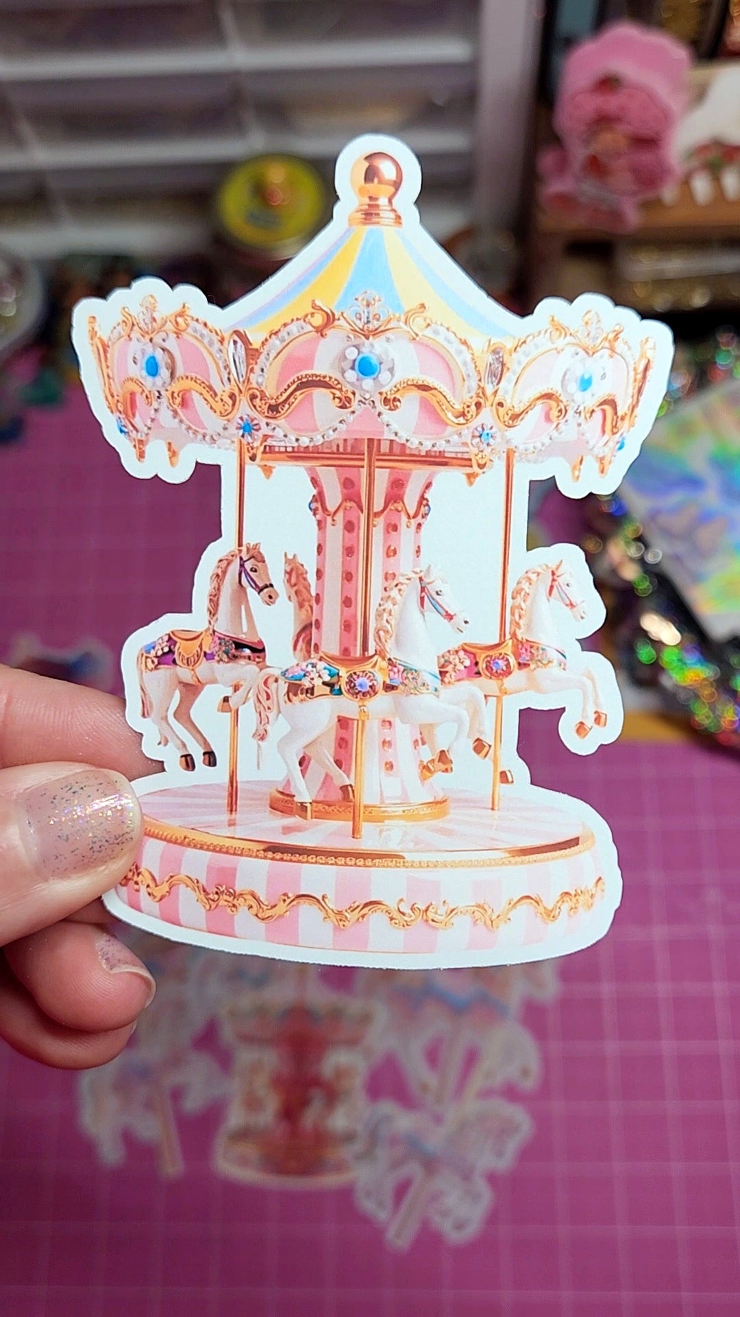 Decorative carousel sticker held by a hand on a pink surface with blurred background