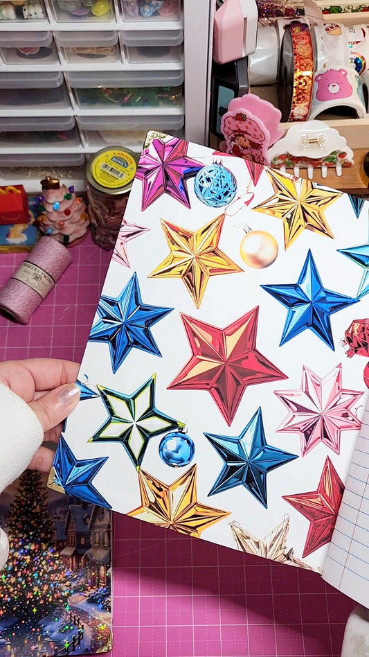 Colorful star-shaped decorations on a white card held by a hand, with a craft room in the background.