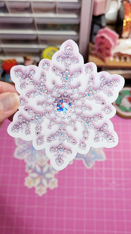 Decorative snowflake sticker with rhinestones held over a pink background