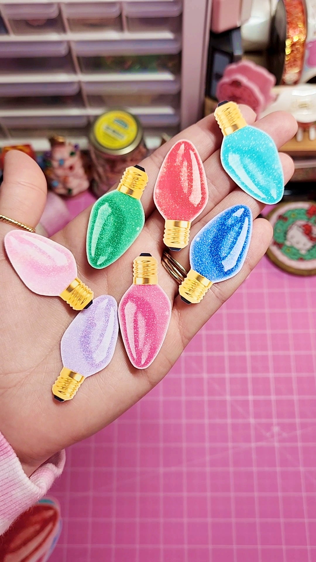 Colorful light bulb-shaped pins held in a hand with a pink grid background
