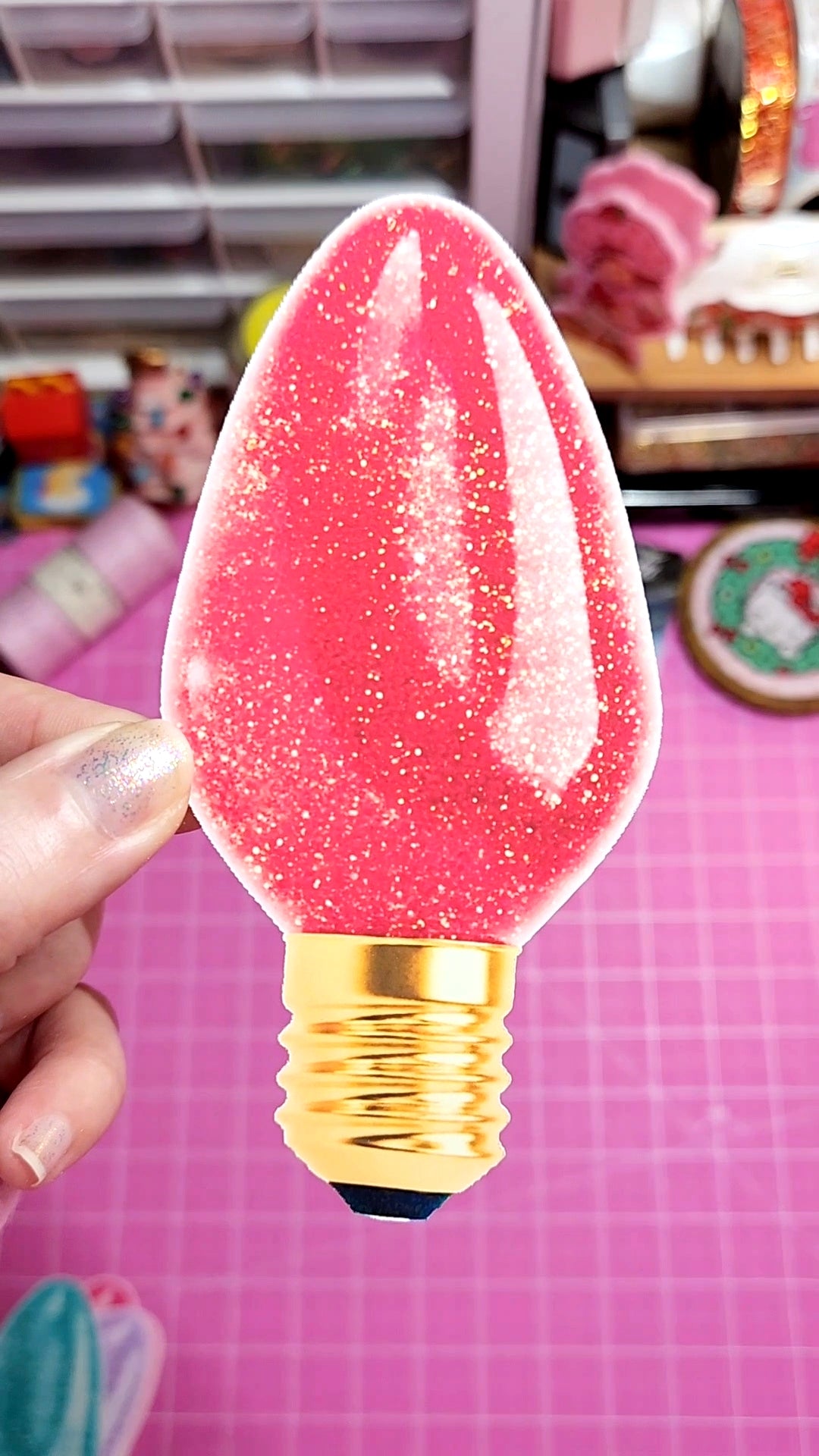 Decorative light bulb with pink and gold design held by a hand on a checkered background.