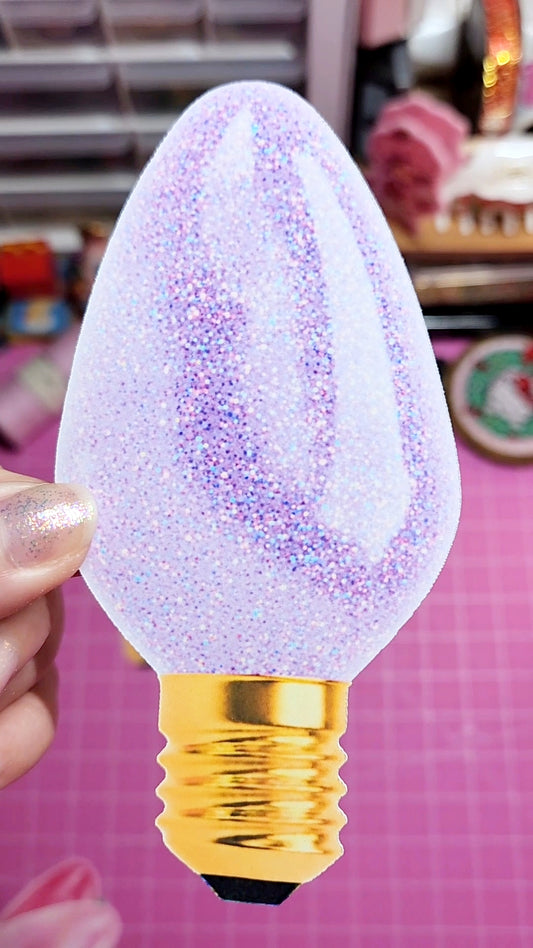 Decorative light bulb with glittery finish held by a hand against a pink background