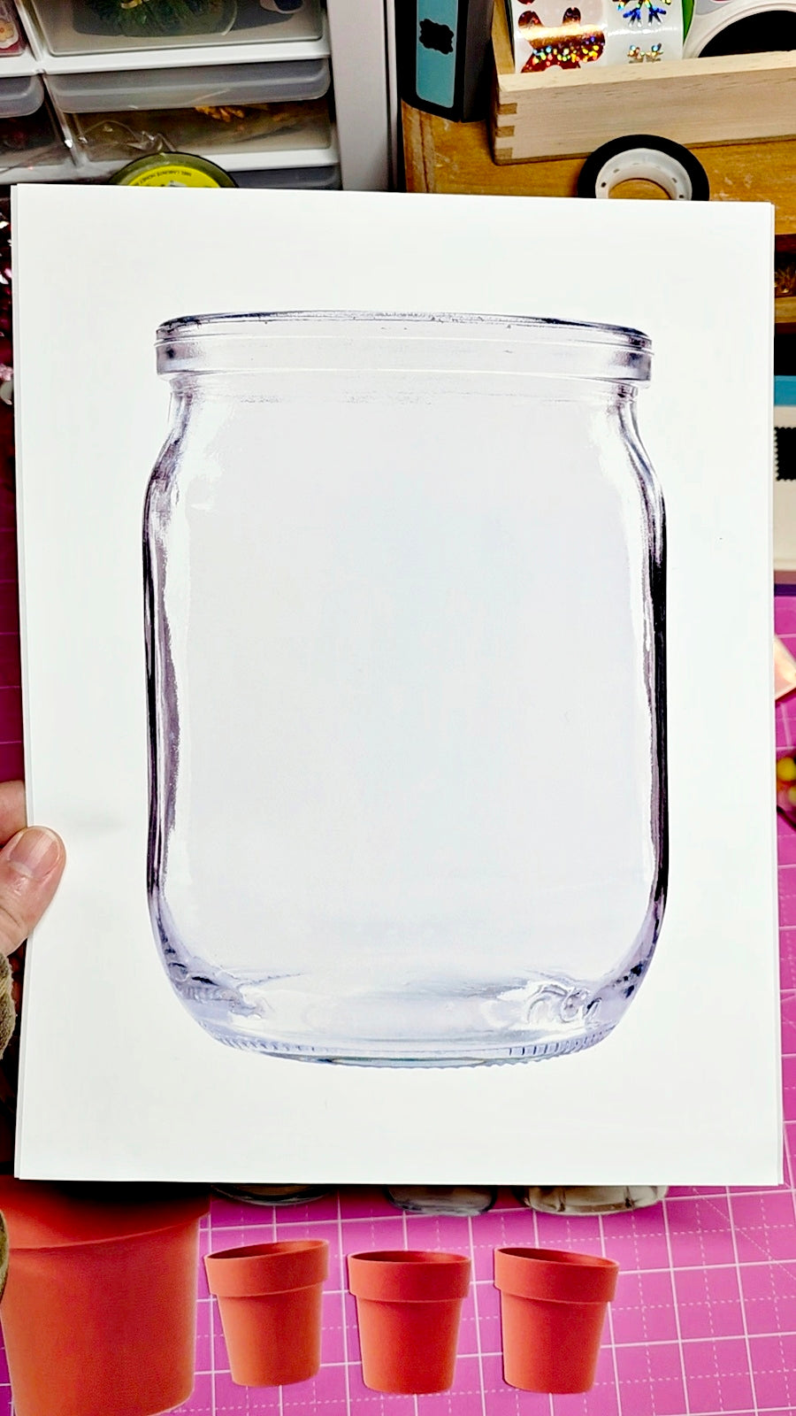 Clear glass jar on a white background with terracotta pots below.