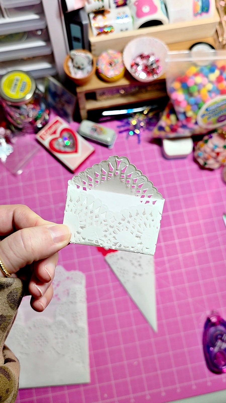 Hand holding a decorative paper cutout on a pink cutting mat with craft supplies in the background.
