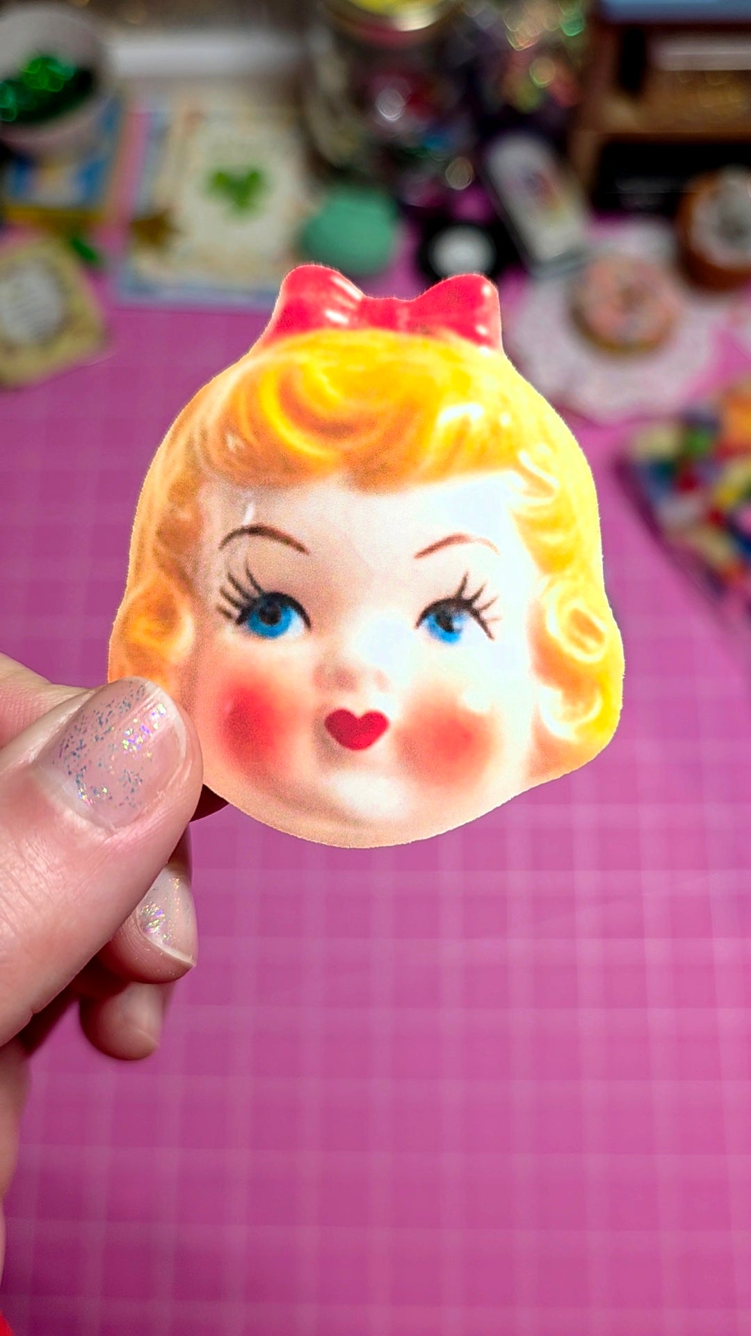 Vintage-style girl's face figurine held by a hand on a pink background