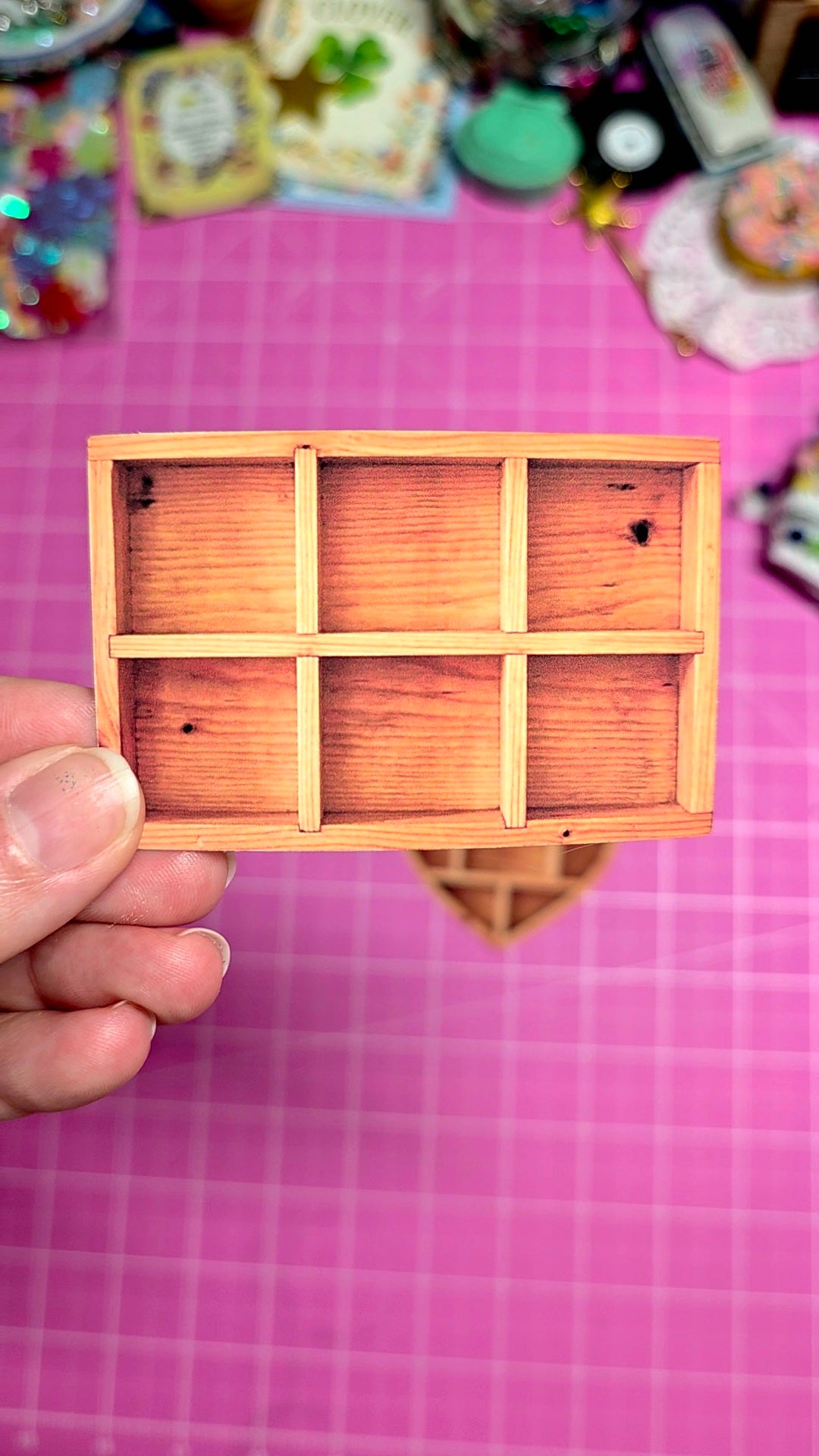 Small wooden box with compartments held by a hand on a pink grid background