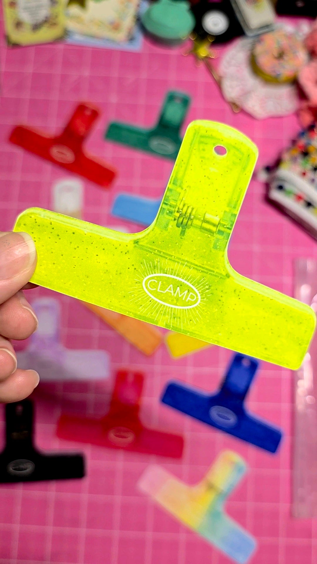 Green letter 'L' shaped tool held by a hand on a pink surface with colorful letters and shapes.