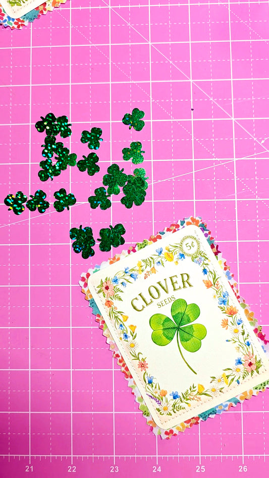 Green shamrock stickers on a pink cutting mat with a floral design and 'Clover' text.