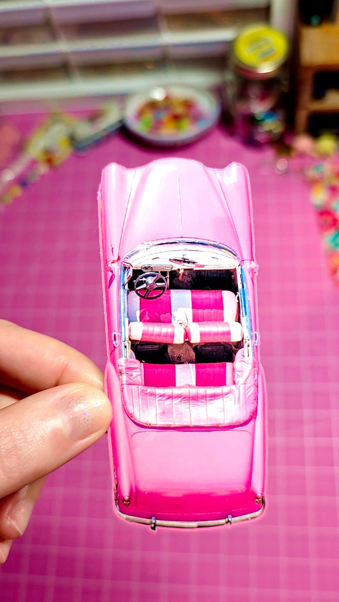 Pink toy car held by a hand on a pink checkered surface.