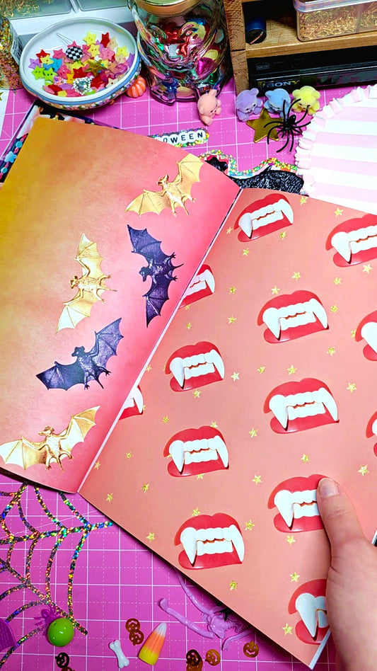 A colorful Halloween-themed scrapbook paper sheet from 'Baby Pickle Shop' surrounded by various Halloween decorations, including plastic bats, a skeleton figure, candy corn, and orange pumpkins, all arranged on a pink cutting mat.
