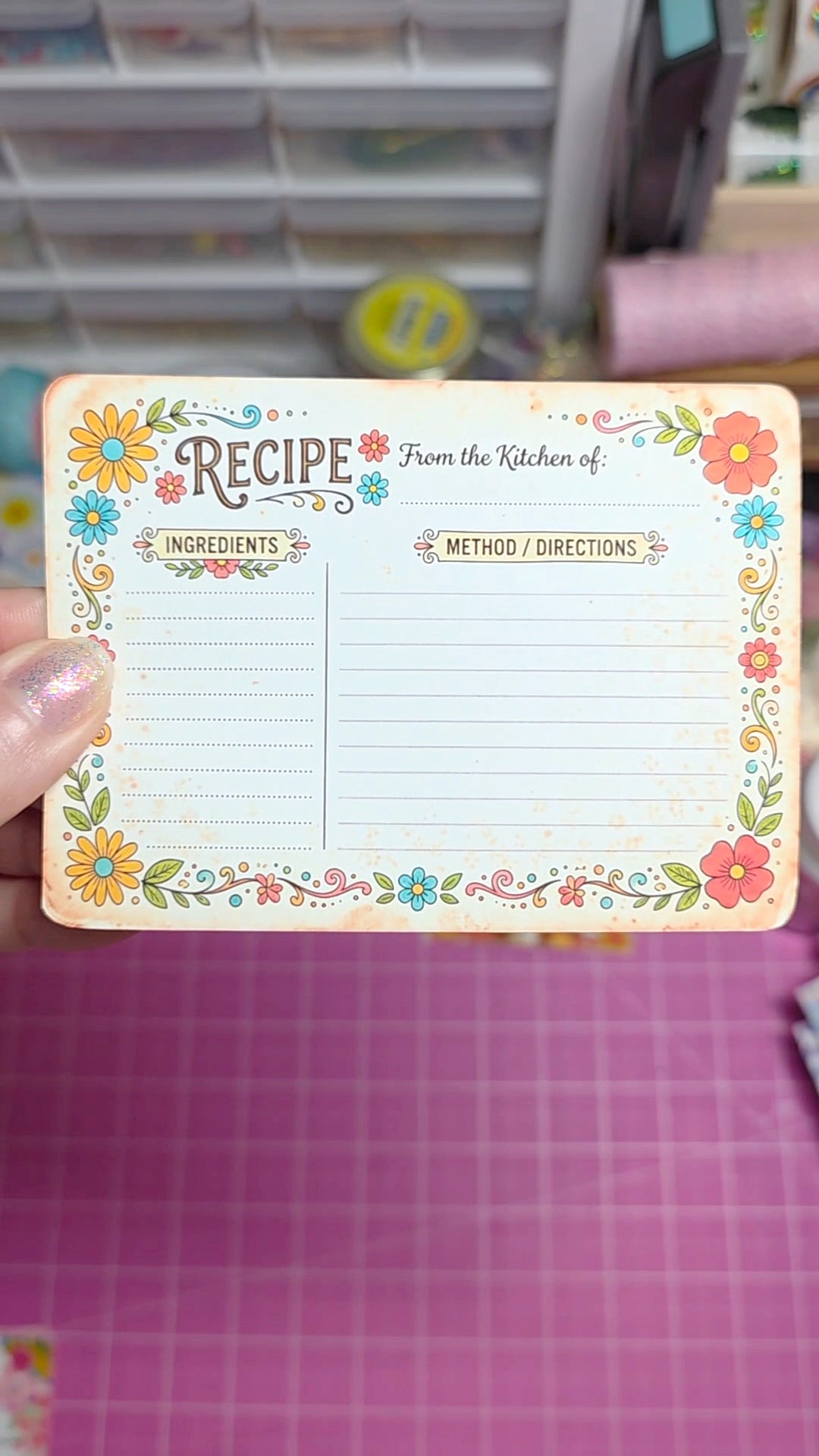 Floral design recipe card held by a hand on a pink surface