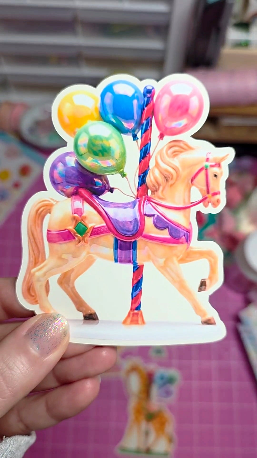 Decorative candle with a horse and balloons design held by a hand.