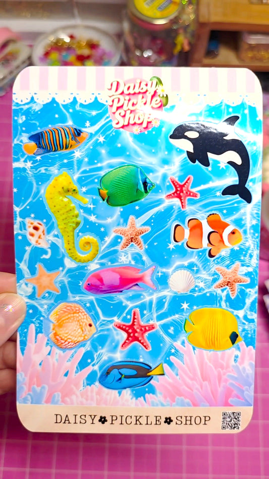 Card with colorful underwater-themed stickers featuring fish, seahorses, and starfish on a blue background.