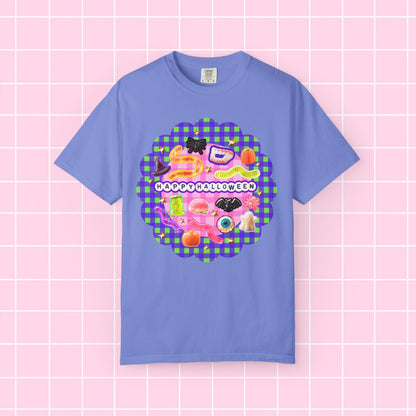 A light blue short-sleeve t-shirt with a colorful 'Happy Halloween' graphic on the chest, displayed against a pink grid background.