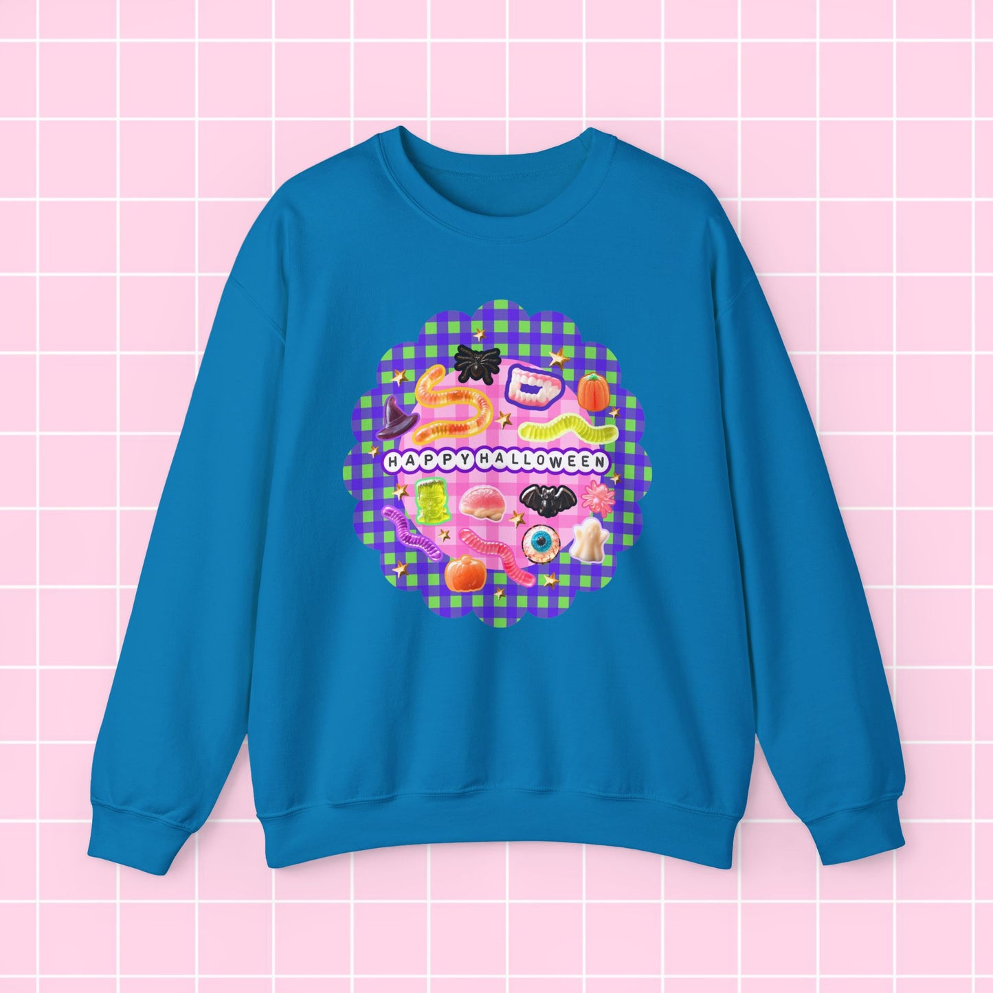 A bright blue crewneck sweatshirt featuring a colorful retro graphic with the text 'HAPPY BLESSING' and a pink gingham pattern, displayed on a pink grid background.