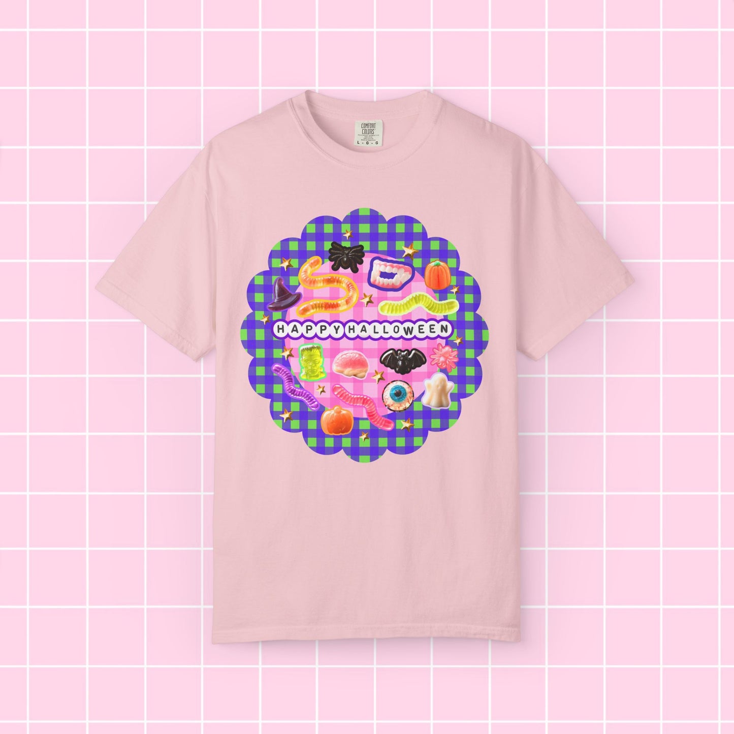 A light pink short-sleeve t-shirt with a colorful 'Happy Halloween' graphic on the chest, displayed against a pink grid background.