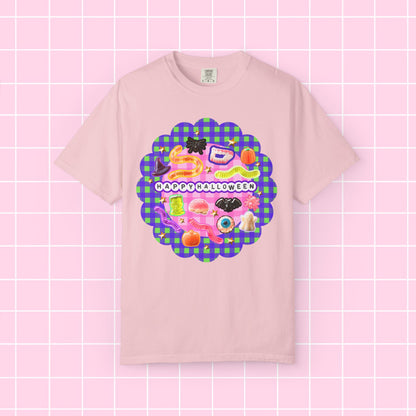 A light pink short-sleeve t-shirt with a colorful 'Happy Halloween' graphic on the chest, displayed against a pink grid background.