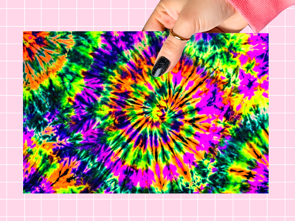 A hand with black glitter nail polish points to a bright neon tie-dye spiral pattern on a rectangular card, set against a pink grid background.