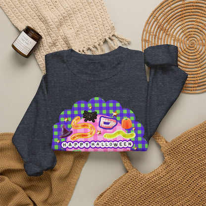 A dark heather gray sweatshirt with a colorful 'Happy Halloween' graphic print, styled in a flat lay with a beige knit blanket, a small candle, and a woven placemat.