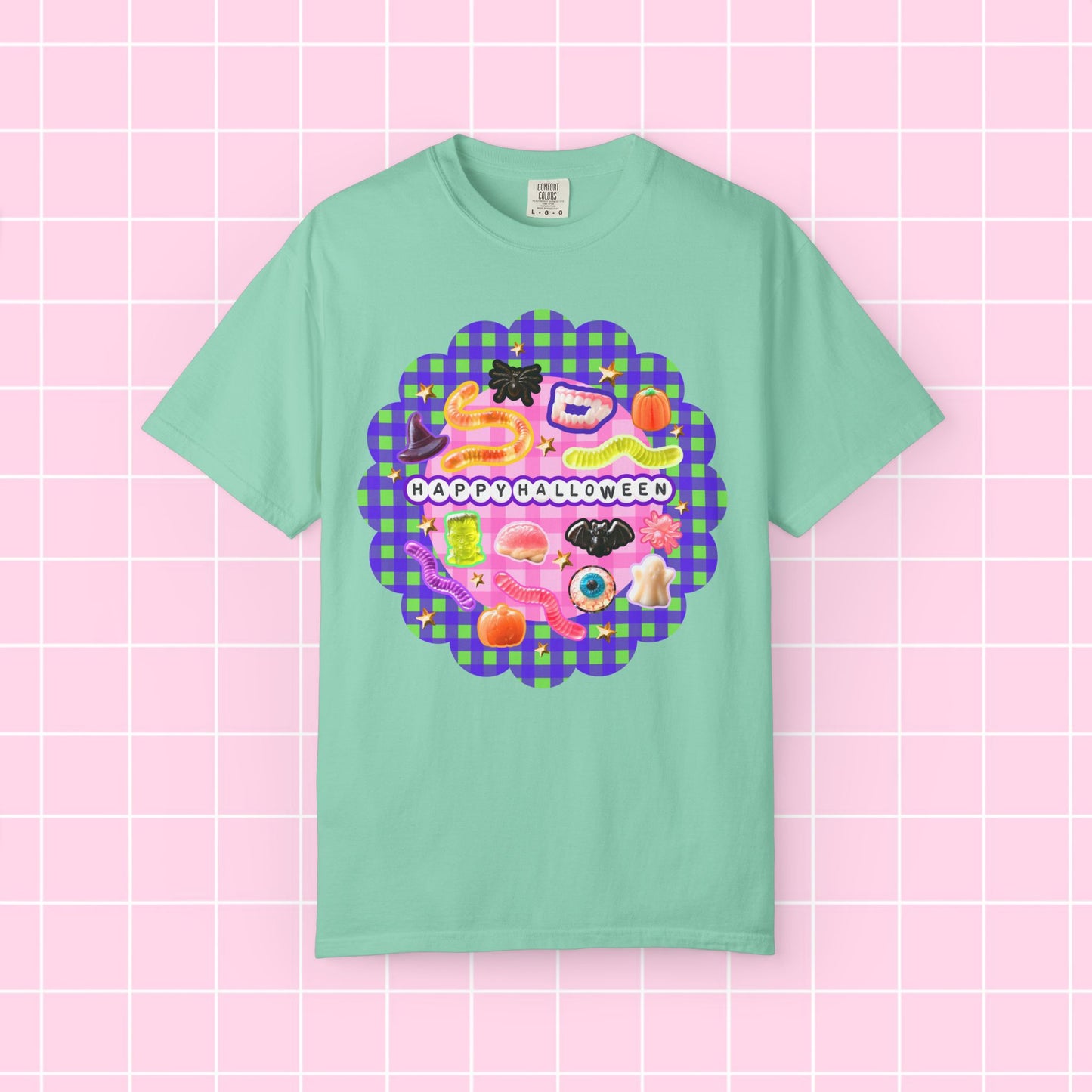 A mint green short-sleeve t-shirt with a colorful 'Happy Halloween' graphic on the chest, displayed against a pink grid background.