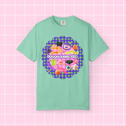 A mint green short-sleeve t-shirt with a colorful 'Happy Halloween' graphic on the chest, displayed against a pink grid background.