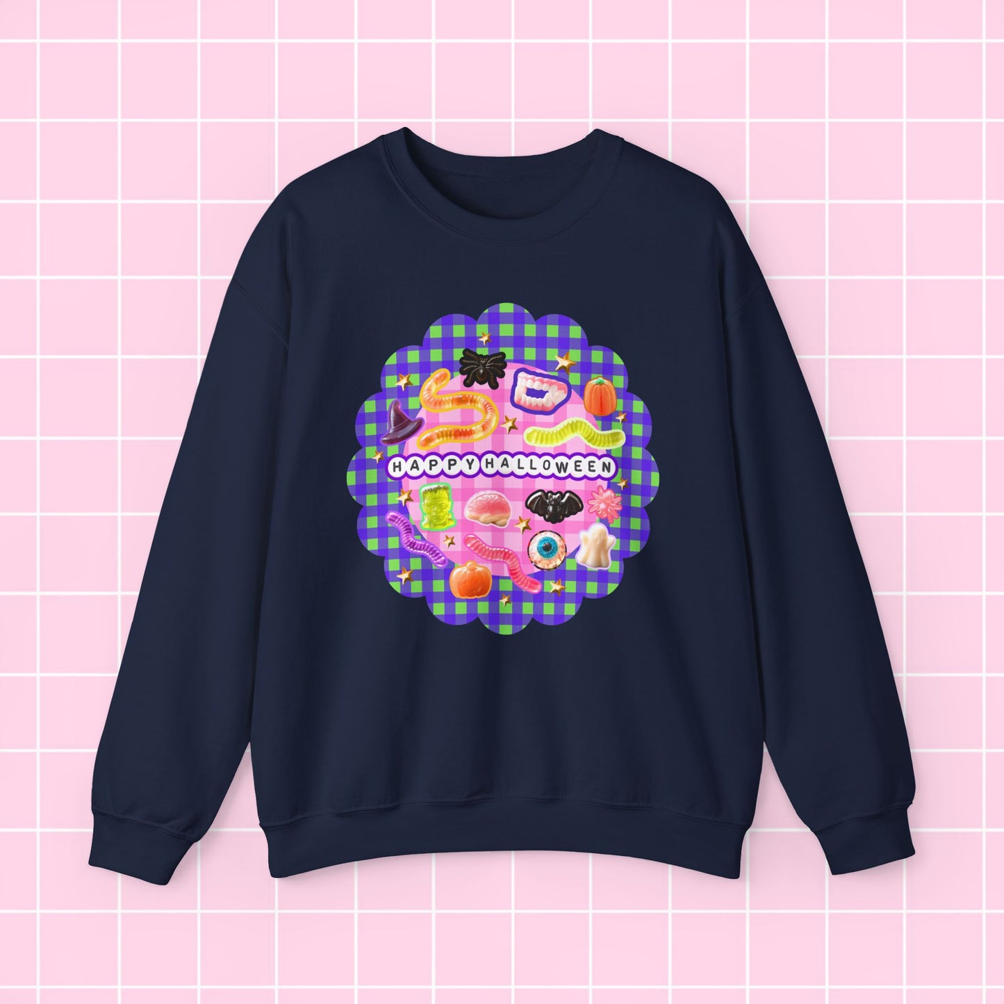 A navy blue crewneck sweatshirt featuring a colorful retro-style graphic on the chest with the text 'HAPPY BLESSING YOU' and a pink and purple gingham scalloped border, displayed against a pink grid background.