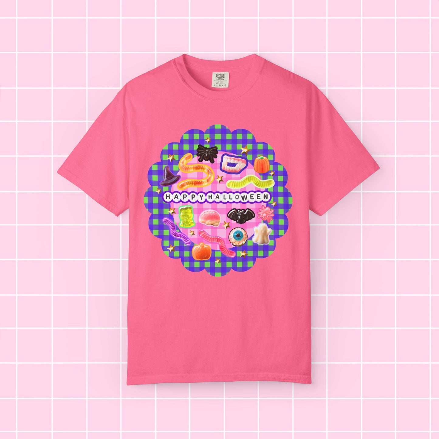 A pink short-sleeve crewneck t-shirt featuring a colorful 'Happy Halloween' graphic on the chest, displayed against a pink grid background.