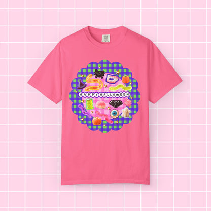 A pink short-sleeve crewneck t-shirt featuring a colorful 'Happy Halloween' graphic on the chest, displayed against a pink grid background.