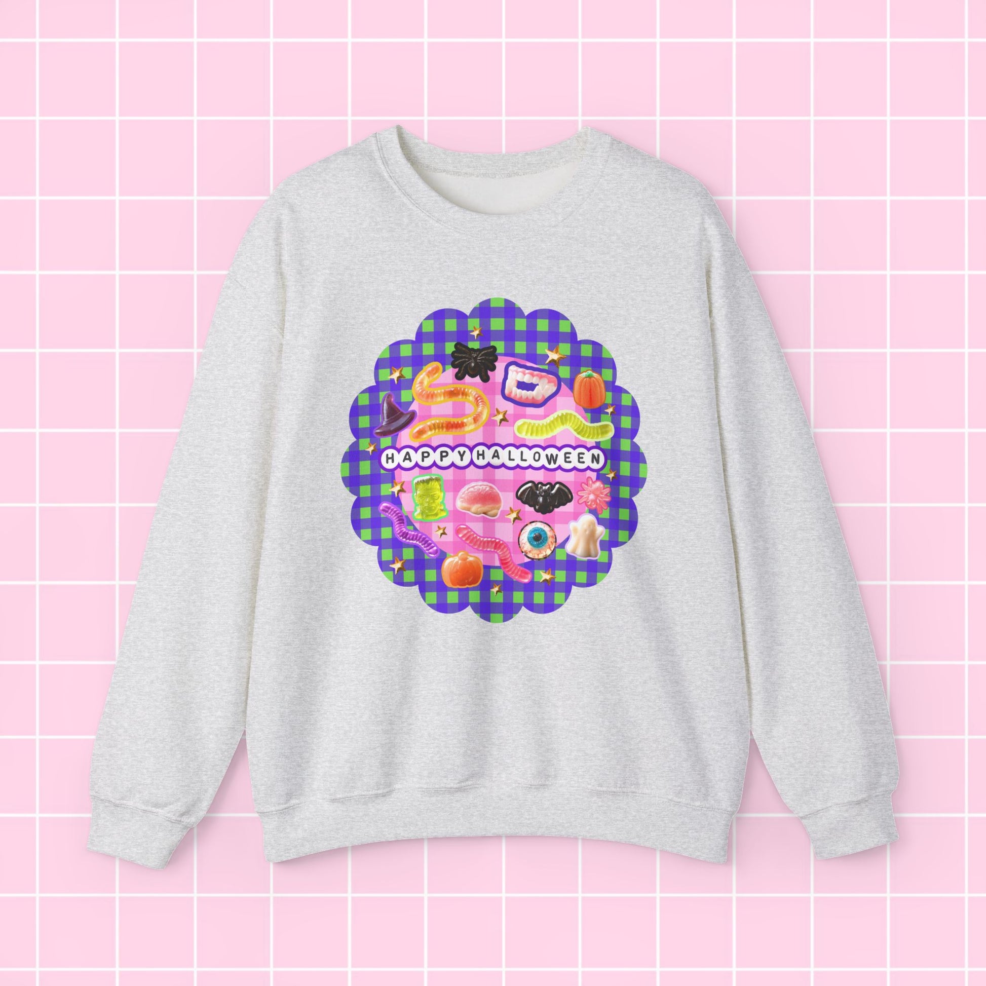 A light heather gray crewneck sweatshirt featuring a colorful retro graphic with the text 'HAPPY BIRTHDAY' on a pink and purple plaid scalloped background, displayed against a pink grid backdrop.