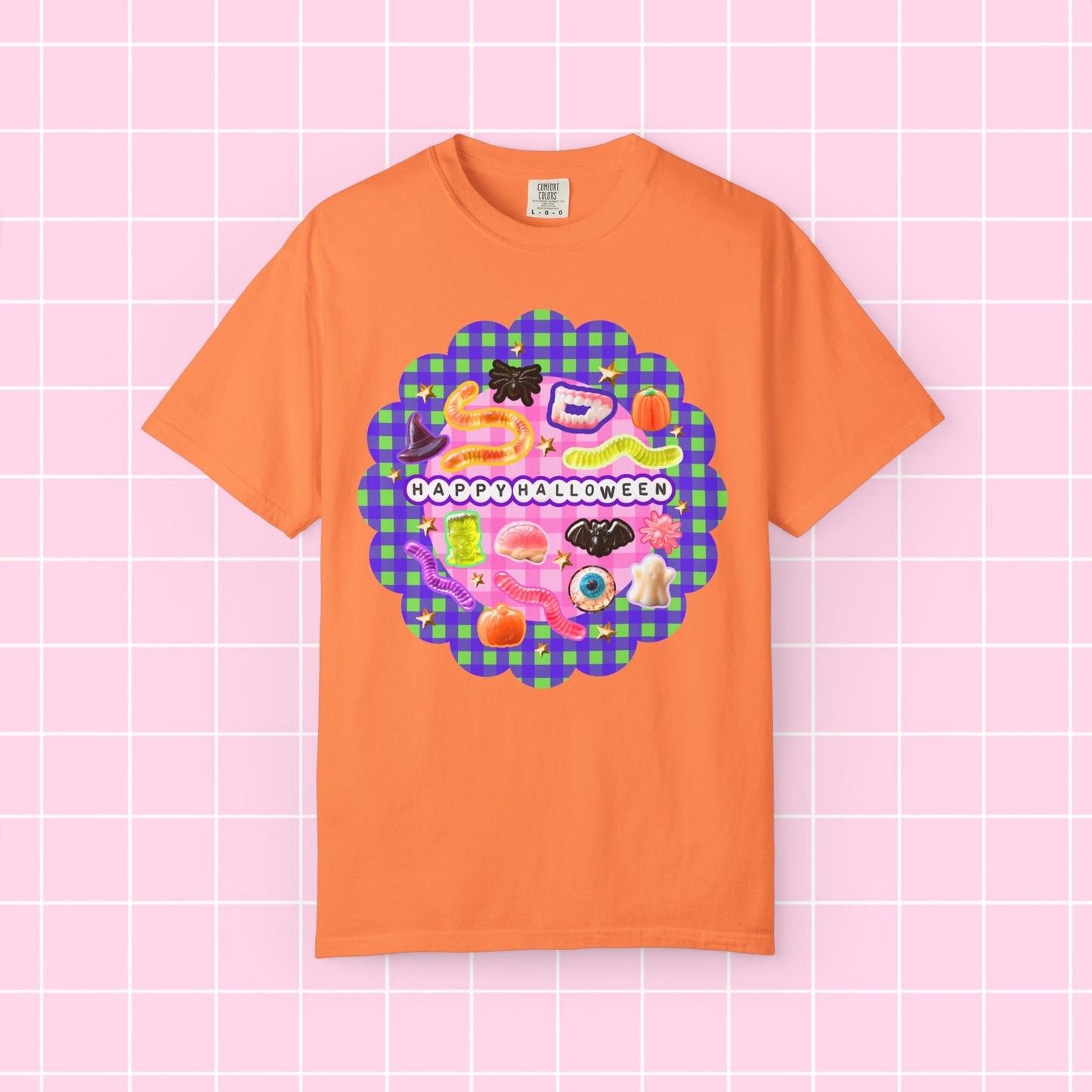 An orange short-sleeve crewneck t-shirt featuring a colorful 'Happy Halloween' graphic print on the front, displayed against a pink grid background.