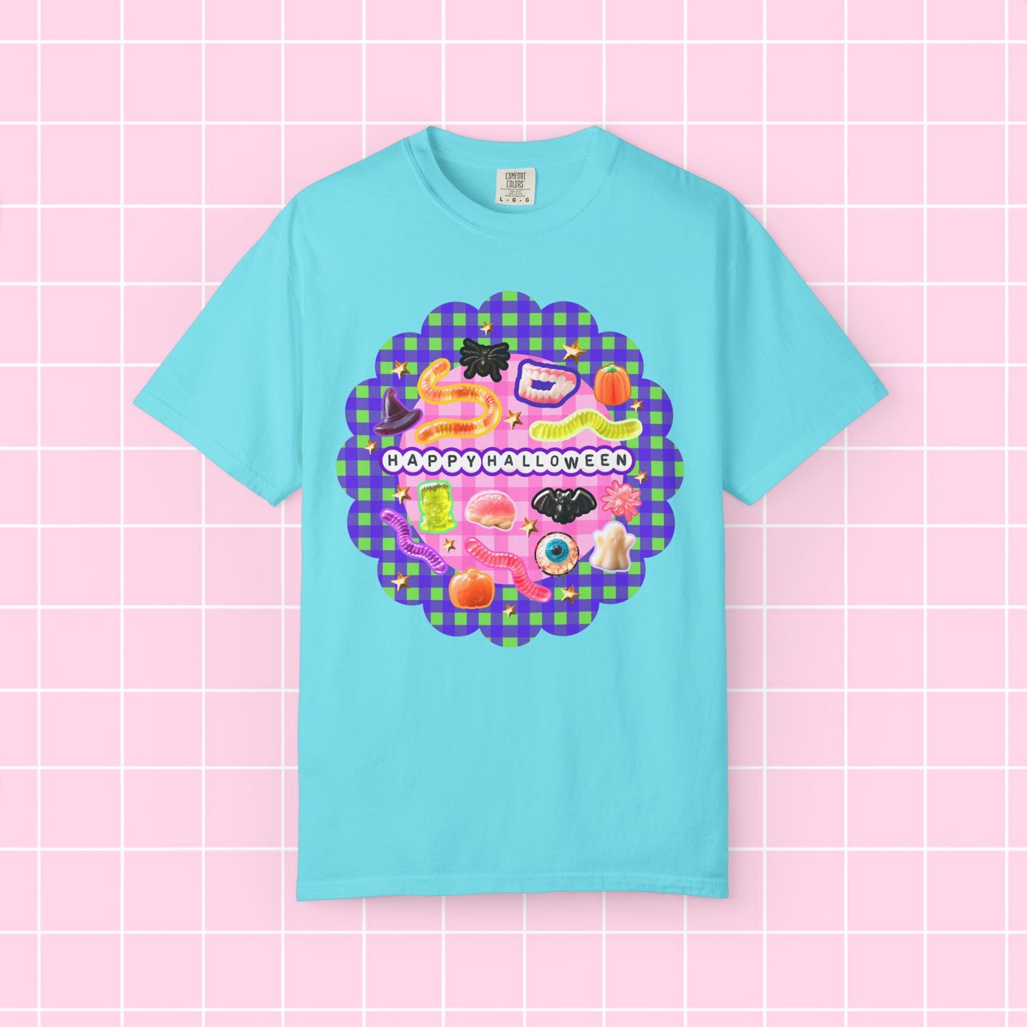 A light blue short-sleeve t-shirt with a colorful 'Happy Halloween' graphic on the chest, displayed against a pink grid background.
