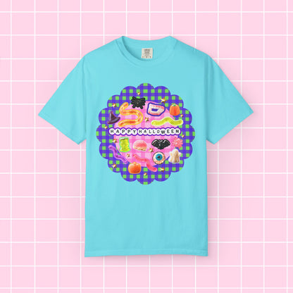 A light blue short-sleeve t-shirt with a colorful 'Happy Halloween' graphic on the chest, displayed against a pink grid background.