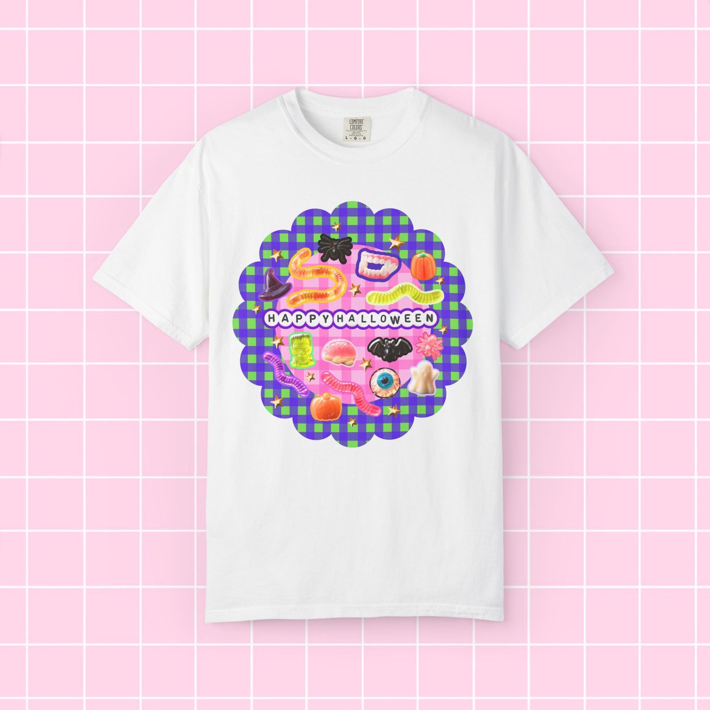 A white short-sleeve crewneck t-shirt featuring a colorful 'Happy Halloween' graphic print on the front, displayed against a pink grid background.
