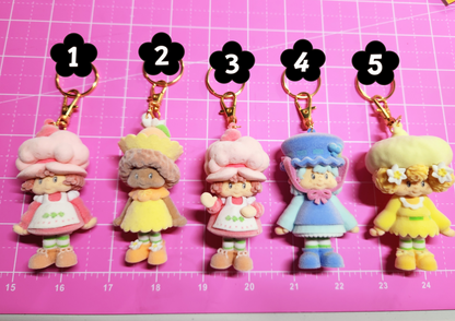 Five cartoon character keychains on a pink grid background
