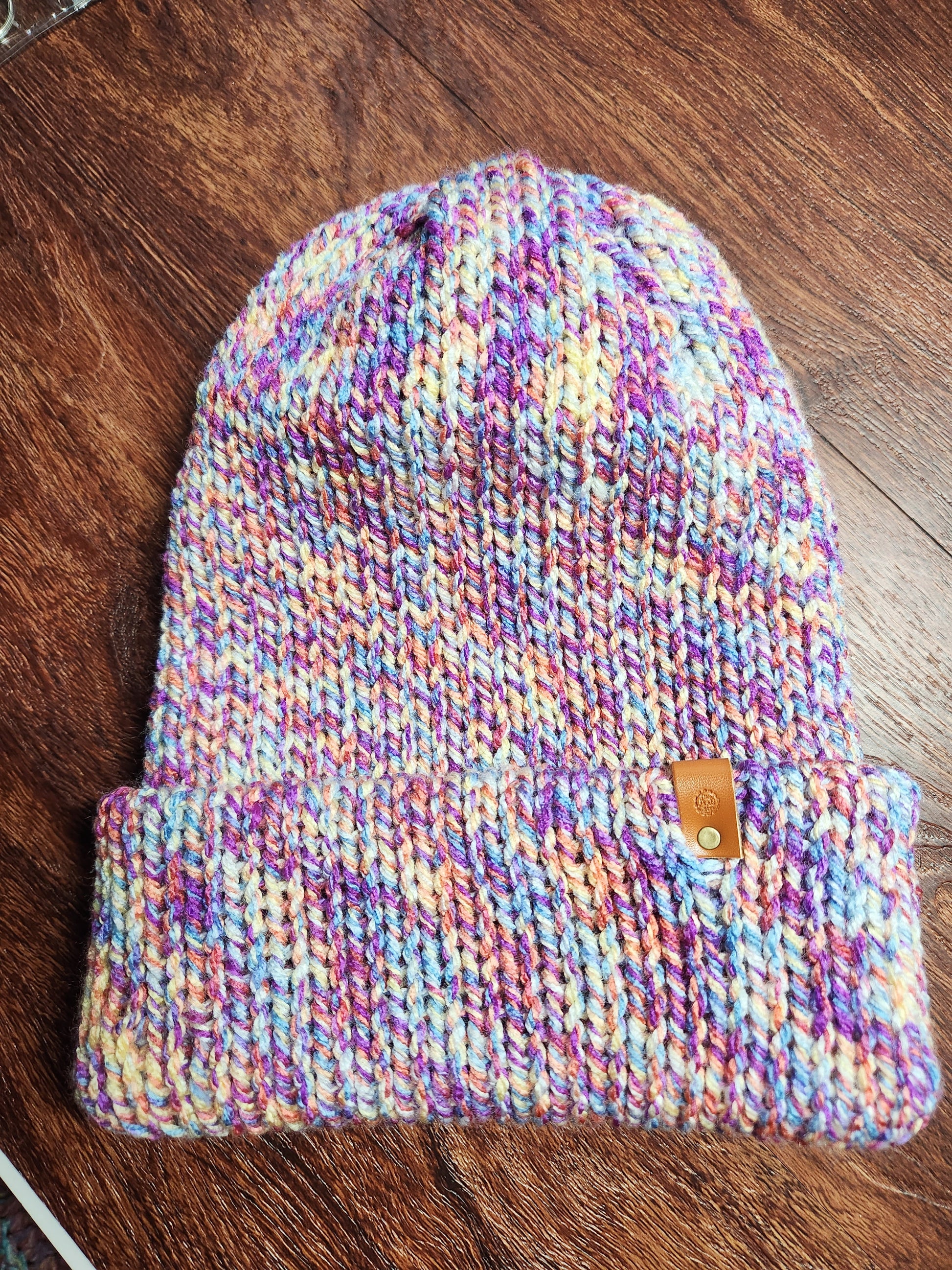 Multicolored knit beanie with a brown button on a wooden surface