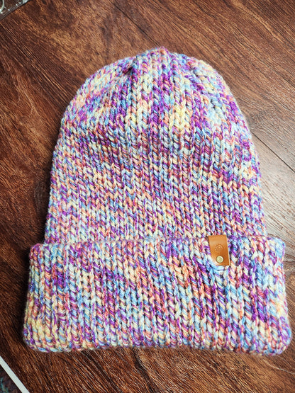 Multicolored knit beanie with a brown button on a wooden surface